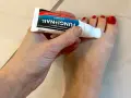 Dłoń aplikuje maść Fungi Nail na paznokcie u stóp. Preparat, podobny do żelu, zawiera metronidazol, pomagając w walce z grzybicą.