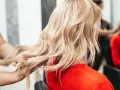 Fryzjerka pokazuje klientce, jak obciąć włosy, prezentując pasmo blond włosów.