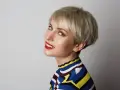 Kobieta z blond fryzurą pixie, która dodaje objętości cienkim włosom. Uśmiecha się, ma na sobie kolorowy sweter.