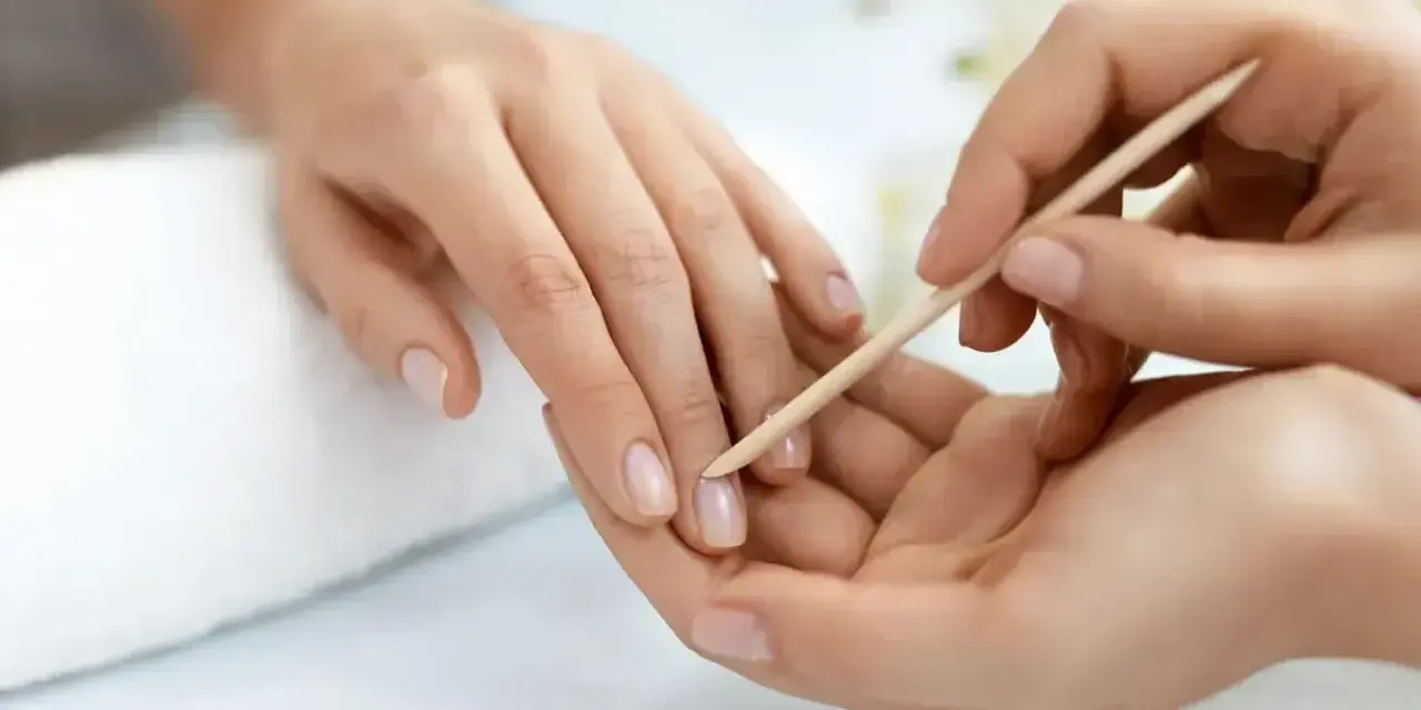 Delikatne dłonie poddawane zabiegowi manicure biologicznego. Drewniany patyczek delikatnie odsuwa skórki, przygotowując paznokcie do dalszych pielęgnacji.