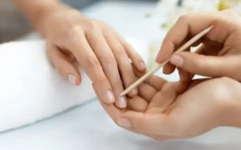Delikatne dłonie poddawane zabiegowi manicure biologicznego. Drewniany patyczek delikatnie odsuwa skórki, przygotowując paznokcie do dalszych pielęgnacji.