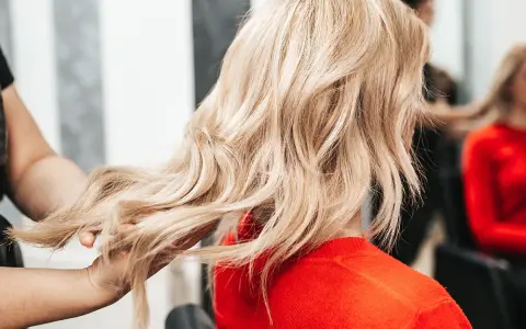 Fryzjerka pokazuje klientce, jak obciąć włosy, prezentując pasmo blond włosów.