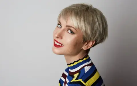Kobieta z blond fryzurą pixie, która dodaje objętości cienkim włosom. Uśmiecha się, ma na sobie kolorowy sweter.