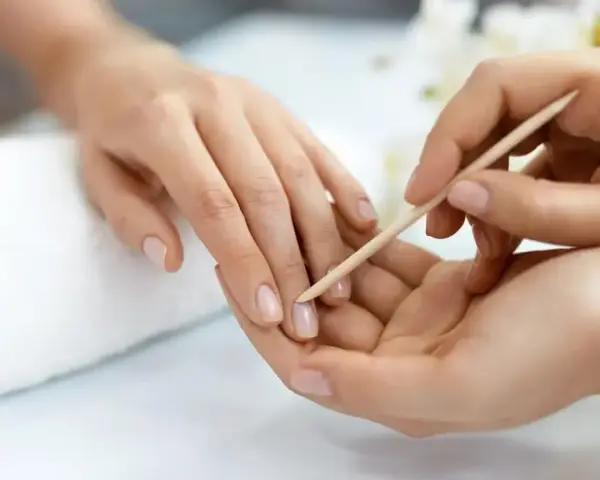 Delikatne dłonie poddawane zabiegowi manicure biologicznego. Drewniany patyczek delikatnie odsuwa skórki, przygotowując paznokcie do dalszych pielęgnacji.