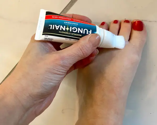 Dłoń aplikuje maść Fungi Nail na paznokcie u stóp. Preparat, podobny do żelu, zawiera metronidazol, pomagając w walce z grzybicą.