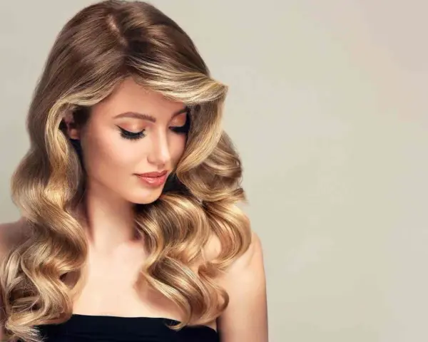 Kobieta z falowanymi, brązowo-blond włosami, delikatnym makijażem i spojrzeniem skierowanym w dół.