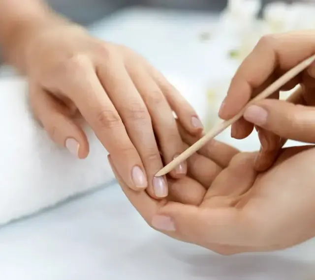 Delikatne dłonie poddawane zabiegowi manicure biologicznego. Drewniany patyczek delikatnie odsuwa skórki, przygotowując paznokcie do dalszych pielęgnacji.