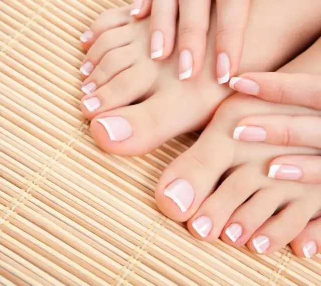 Dłonie i stopy z klasycznym, modnym pedicures. Delikatne paznokcie z białymi końcówkami na bambusowym tle.