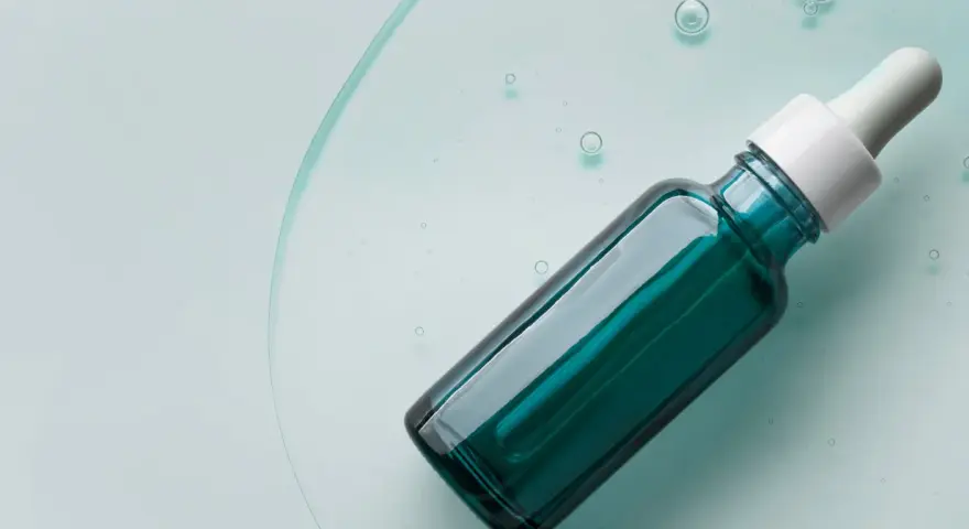 Szklana buteleczka z pipetką, wypełniona zielonym serum, na tle płynu z bąbelkami.