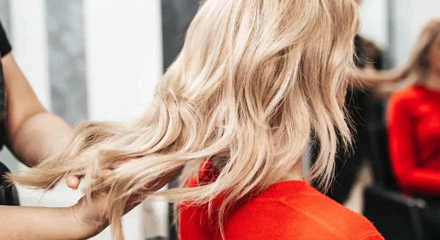 Fryzjerka pokazuje klientce, jak obciąć włosy, prezentując pasmo blond włosów.