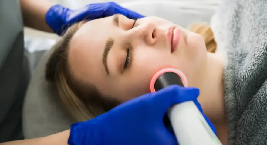 Kobieta przechodzi zabieg geneo. Kosmetolog w niebieskich rękawiczkach wykonuje zabieg na twarzy klientki.