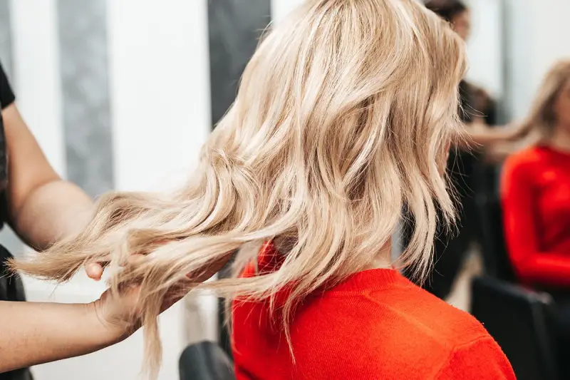Fryzjerka pokazuje klientce, jak obciąć włosy, prezentując pasmo blond włosów.