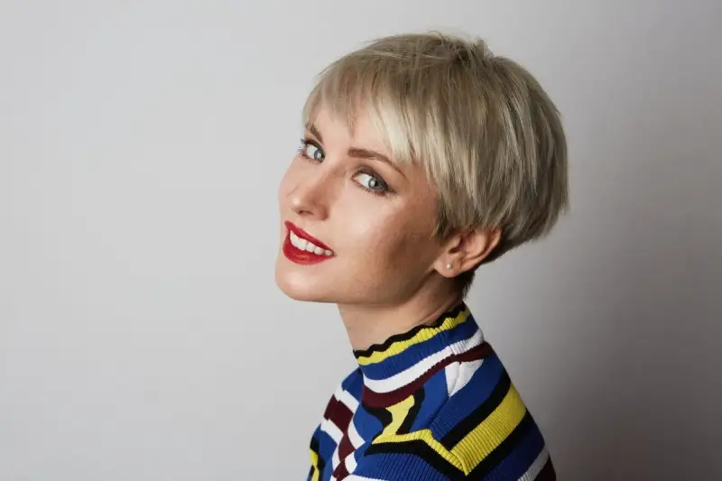 Kobieta z blond fryzurą pixie, która dodaje objętości cienkim włosom. Uśmiecha się, ma na sobie kolorowy sweter.