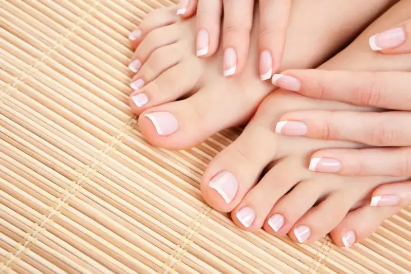 Dłonie i stopy z klasycznym, modnym pedicures. Delikatne paznokcie z białymi końcówkami na bambusowym tle.